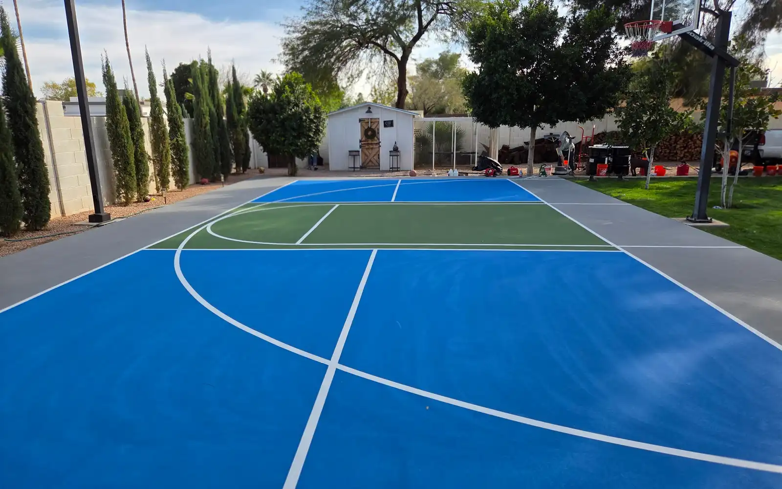 Blue and green backyard basketball court beside cypress trees in Arizona